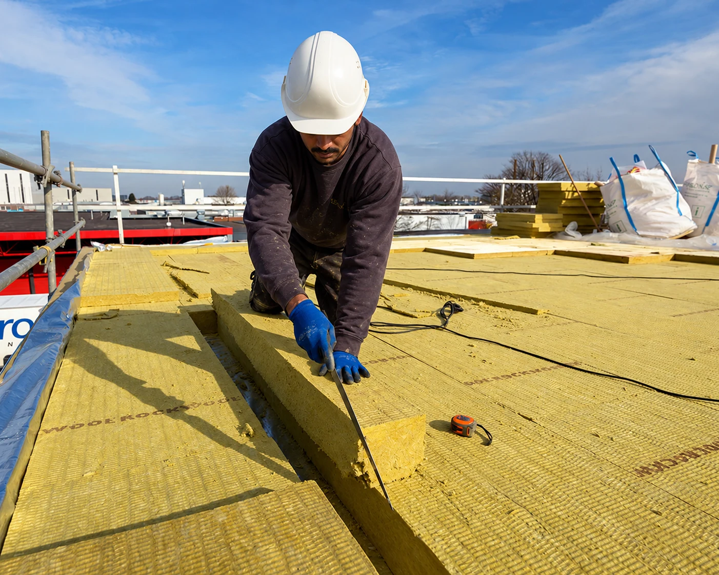 Worker wearing a safety helmet and protective gloves, cutting stone wool insulation on a roof